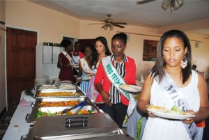 : Lunch is served: Miss St. Kitts, Pernelle Abraham, and behind her, Miss Montserrat, Vanice Tuitt, and others by the buffet table.