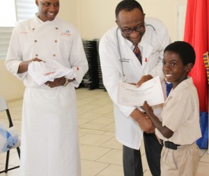 Head of the Rouse Foundation, Cardiologist Dr. Charlie Rouse and Celebrity Chief of Atlanta Marvin Woods, distribute Certificates of Participation and chief gear to students of the Charlestown Primary School for their participation in the Mini Chief Academy on February 24, 2015 