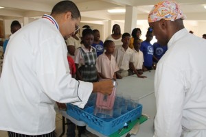 (L-R) Food and Nutrition Specialist attached to the School Meals Programme on Nevis, Executive Chef Michael Henville and Celebrity Chief of Atlanta Marvin Woods, demonstrates to students of the Charlestown Primary School how to make healthy snacks at a Mini Chief Academy session at the school’s kitchen on February 24, 2015