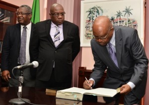 Acting Governor General Seaton signs the legal documents while Prime Minister Harris looks on as Attoney General Vincent Byron shares pleasantries with other Cabinet members