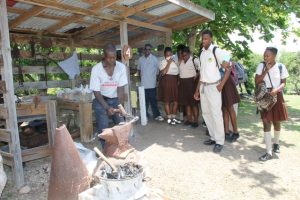 Students of the Gingerland Secondary School looking on as a blacksmith demonstrates how iron objects were made in Nevis yesteryear, at the Ministry of Tourism’s Nevisian Heritage Life at the Nevisian Heritage Village in Zion on May 05, 2016 