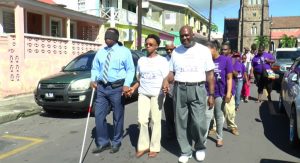 Minister Hamilton (blue attire), plays the role of blind man during an event dubbed ‘Walk a Mile in My Shoes’, which was organised by the Association of Disabled Persons.